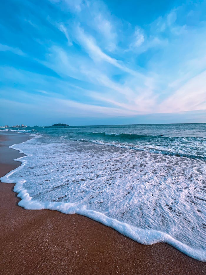 A picturesque view of Mazatlán's beach with waves gently crashing under a vivid blue sky.