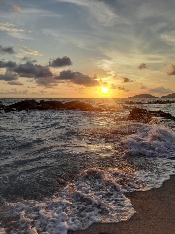 Golden sunset over Mazatlan beach with waves crashing on rocks.