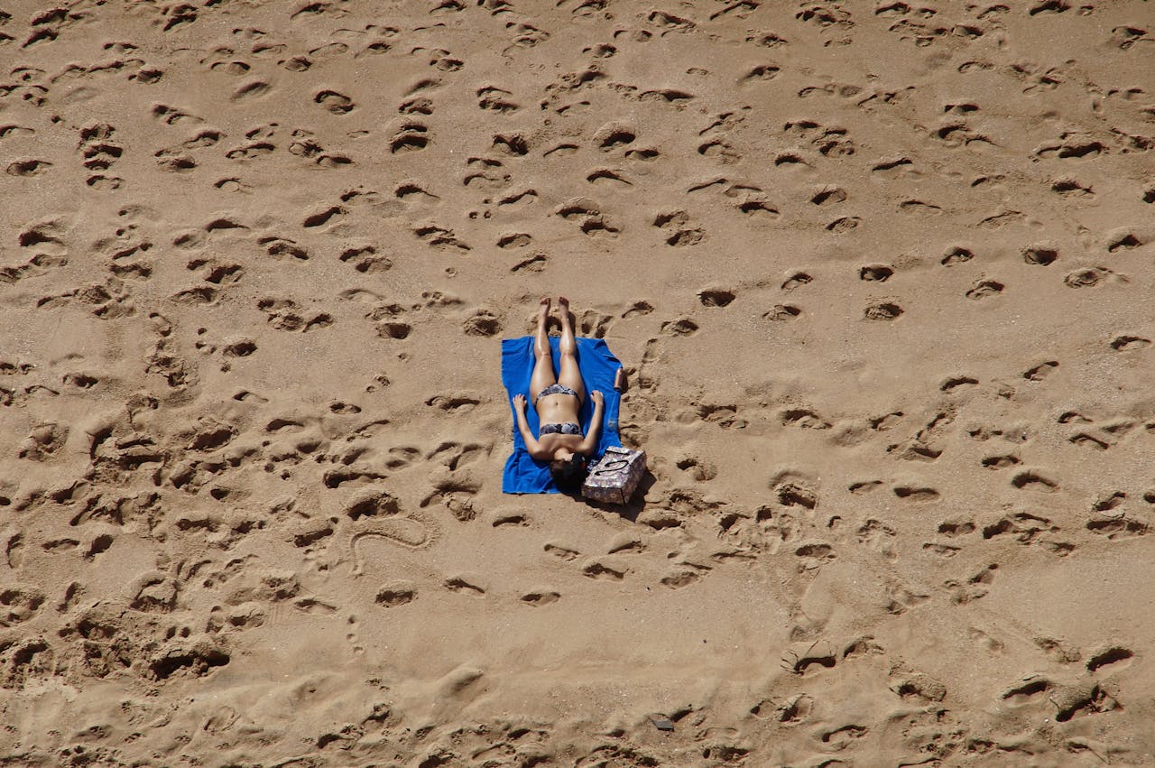 A woman in a bikini sunbathes on a sandy beach in Mazatlán, Mexico, surrounded by footprints.